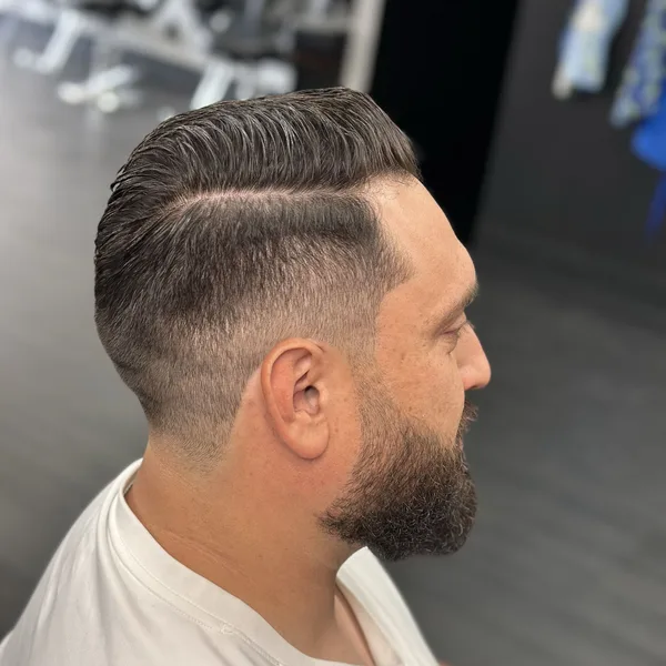 Hard-part comb-over blended into a low fade and shaped beard